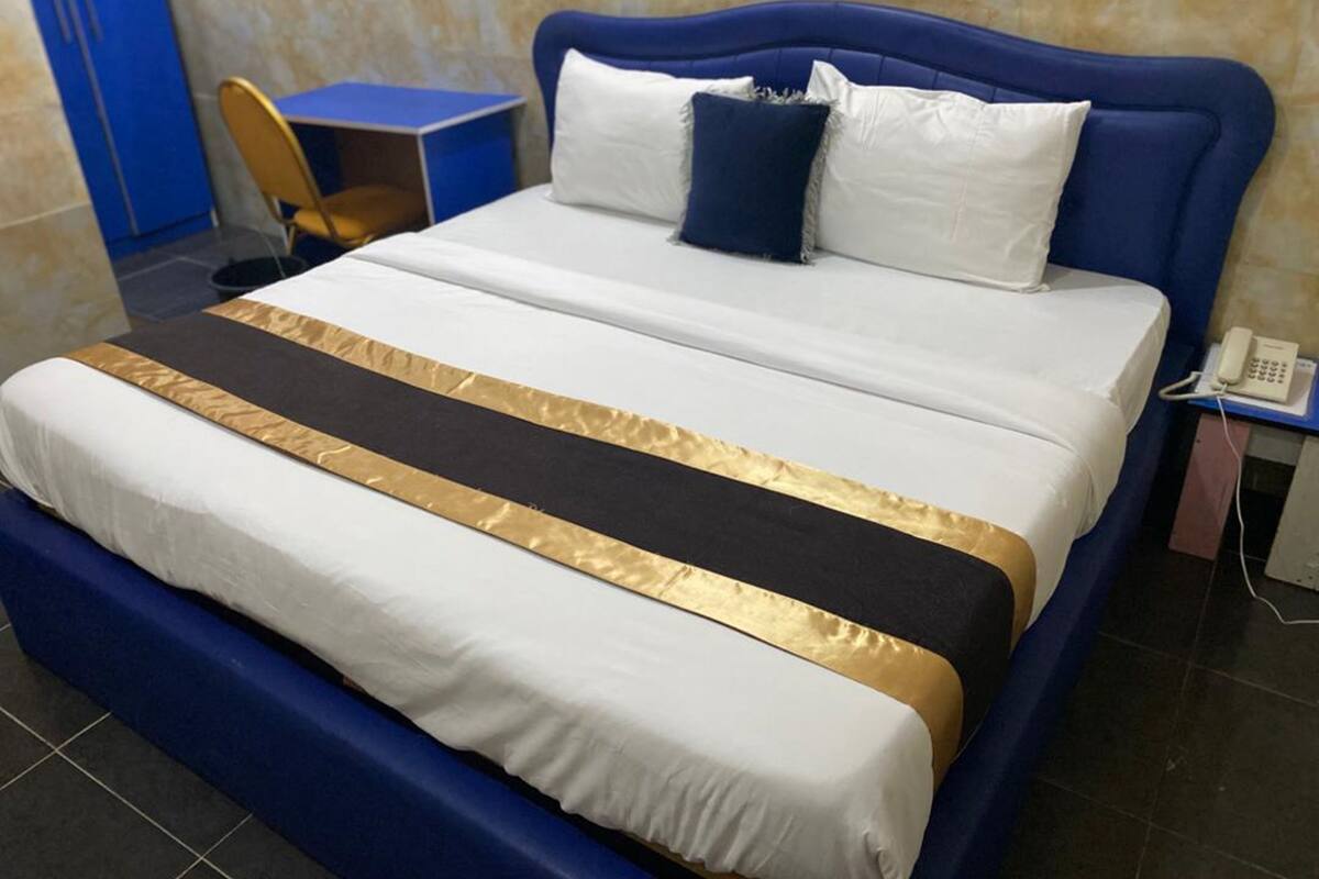 Ein Bett mit blauer Kopfteil, Bettwäsche in Weiß und Gold sowie ein Nachttischtelefon.