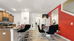 Une cuisine moderne dotée d’un îlot central, d’appareils électroménagers en acier inoxydable et d’un coin repas avec des chaises noires et un mur d’accent rouge.