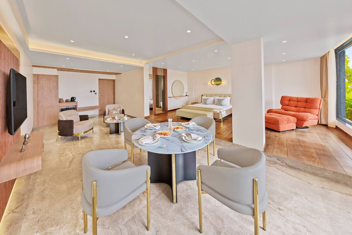 A modern hotel room with a dining area, a sofa, and a TV.