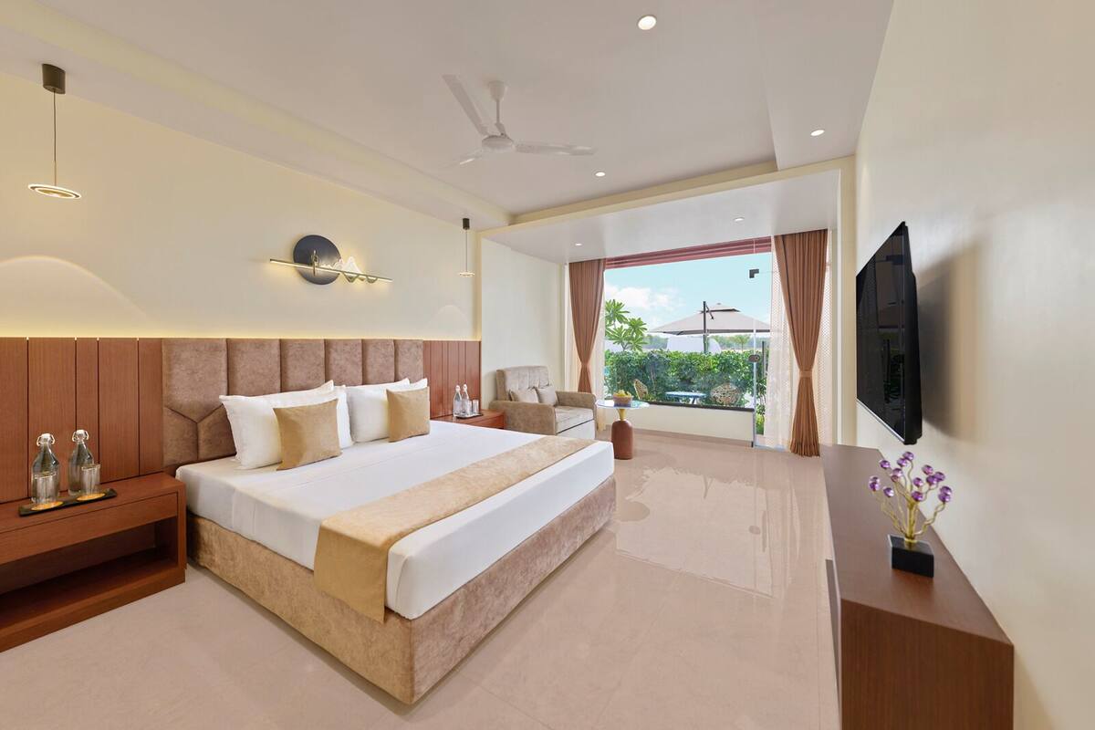 A spacious bedroom with a large bed, a flat-screen TV, a ceiling fan, and a balcony with a view.