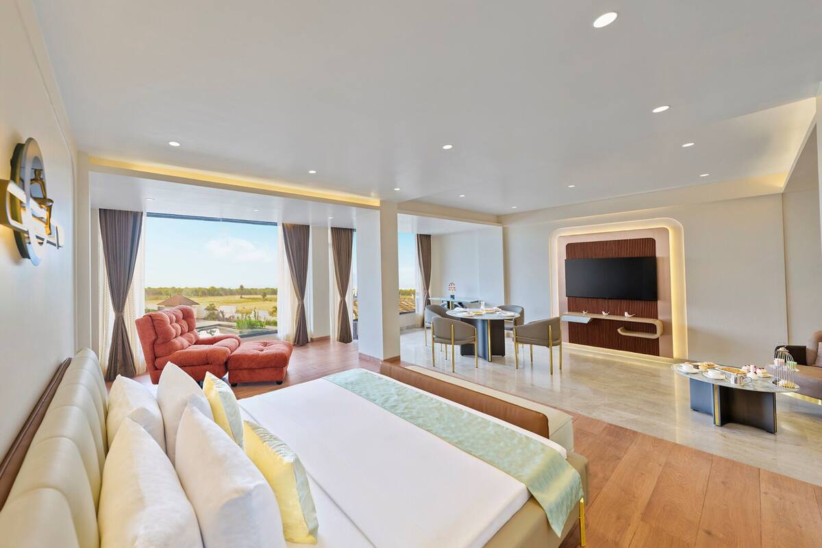 A hotel room with a large bed, a seating area with chairs, a dining table, and a TV.