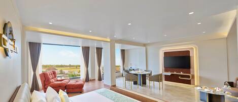 A hotel room with a large bed, a seating area with chairs, a dining table, and a TV.