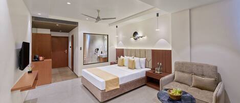 A modern hotel room with a large bed, a sofa, a small round table, a TV, and a mirror.
