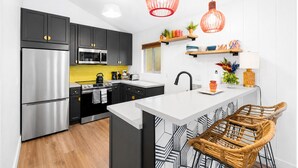 A modern kitchen with dark cabinets, stainless appliances, a yellow backsplash, and a central island with bar stools.