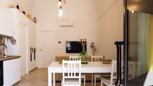A dining area with a white table, chairs, a green vase, and a television on the wall.