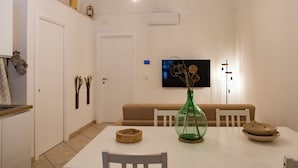 A dining area with a white table, chairs, a green vase, and a television on the wall.