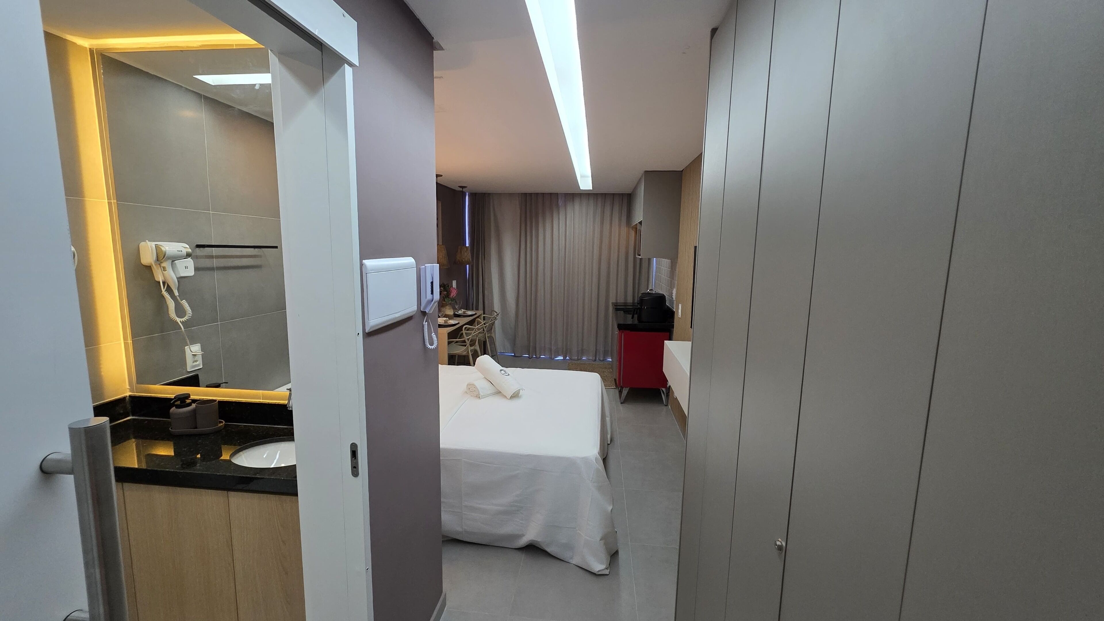 A hotel room with a bed, a desk, a mirror, a vanity with a sink, and a wardrobe.