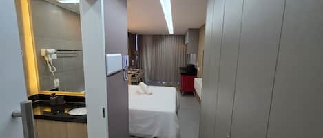 A hotel room with a bed, a desk, a mirror, a vanity with a sink, and a wardrobe.