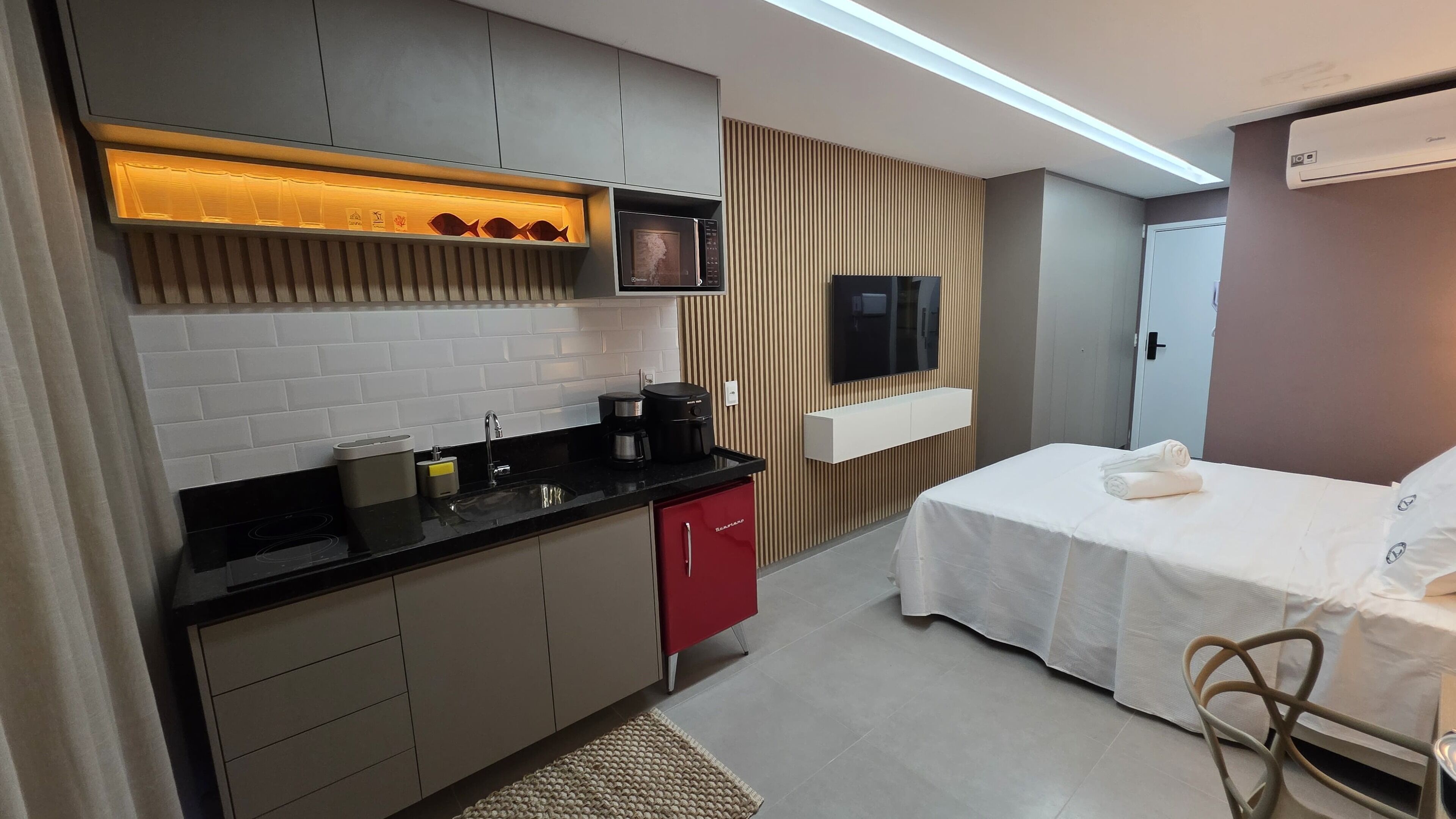 Una habitación de hotel compacta con kitchenette, una cama, un televisor y un armario.