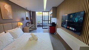 Ένα δωμάτιο ξενοδοχείου με ένα κρεβάτι, ένα κομοδίνο, ένα φωτιστικό, μια τηλεόραση και θέα στο εξωτερικό μπαλκόνι.