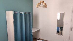 Un dormitorio con cama, escritorio, silla, espejo y cortina de ducha.