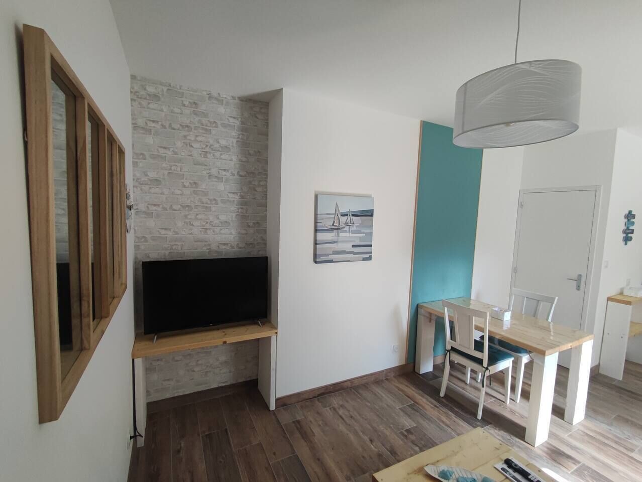 Una sala de estar moderna con un televisor sobre un mueble de madera, una mesa de comedor con sillas, y una lámpara colgante.