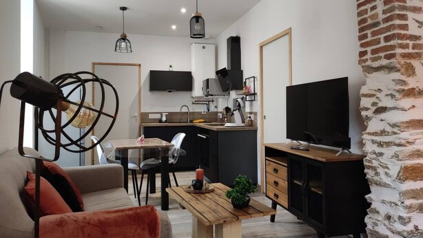 A modern kitchen with a dining area, a TV, and a stone accent wall.