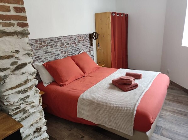 A bedroom with a brick wall, a wooden headboard, a red bedspread, and a white blanket.