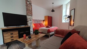 A modern living room with a flat-screen TV, wooden furniture, a brick accent wall, and a cozy seating area with red cushions.