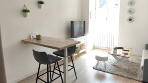 Una cocina moderna con una mesa de madera, dos taburetes altos, un televisor y una pequeña mesa de comedor con un tapete.