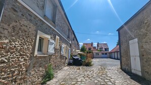 Una estrecha calle adoquinada bordeada por edificios de piedra con puertas y ventanas blancas, que conduce a un edificio más grande en la distancia.