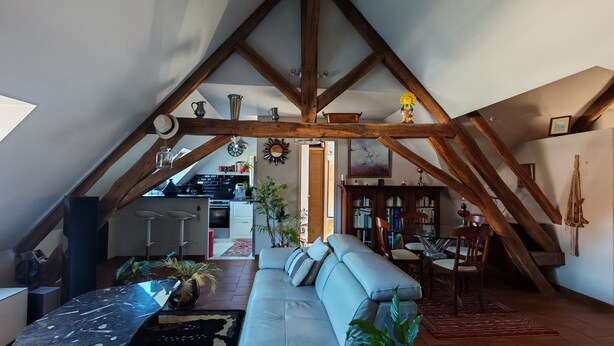 Un espacio habitable tipo loft con vigas de madera a la vista, una cocina y una zona de estar con sofá y sillones.