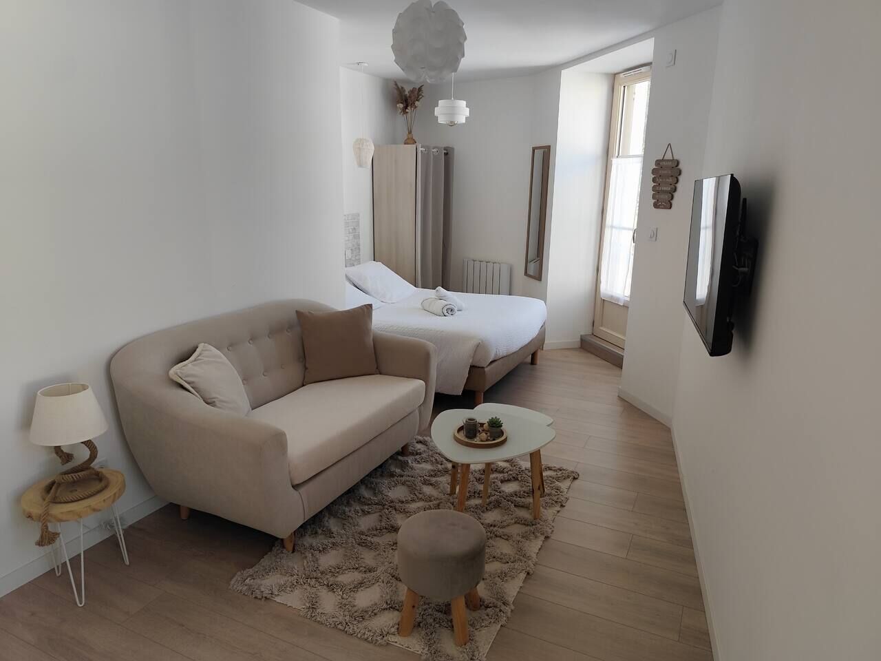 Ein moderner, gut beleuchteter Raum mit einer Couch, einem kleinen runden Tisch, einem dekorativen Teppich und einem Bett mit weißem Kopfteil.