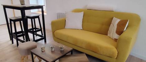 Una sala de estar con un sofá amarillo, una mesita de madera y un taburete a juego.
