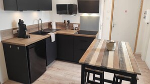 Une cuisine compacte avec des meubles de couleur noire, un plan de travail en bois, un lave-vaisselle encastré et une petite table à manger avec des tabourets.