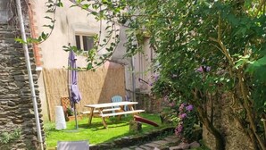 Un jardin avec un mur en pierre, une table en bois et deux chaises en plastique blanches.