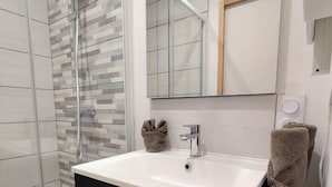 Une salle de bain moderne avec une douche à l’italienne en verre, un lavabo blanc avec un meuble noir et un miroir au-dessus du lavabo.