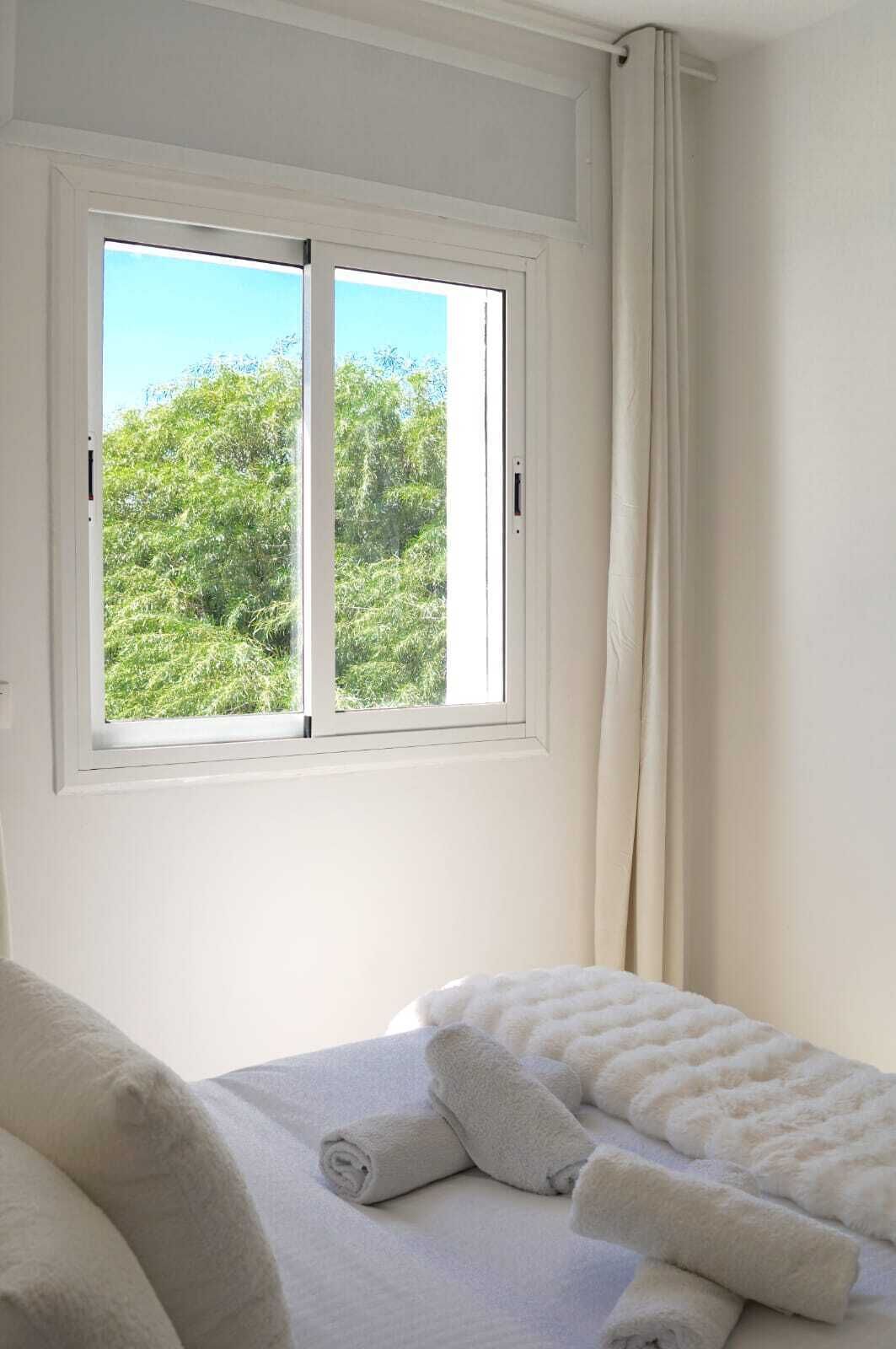 A room with a bed, a window with curtains, and a view of greenery outside.