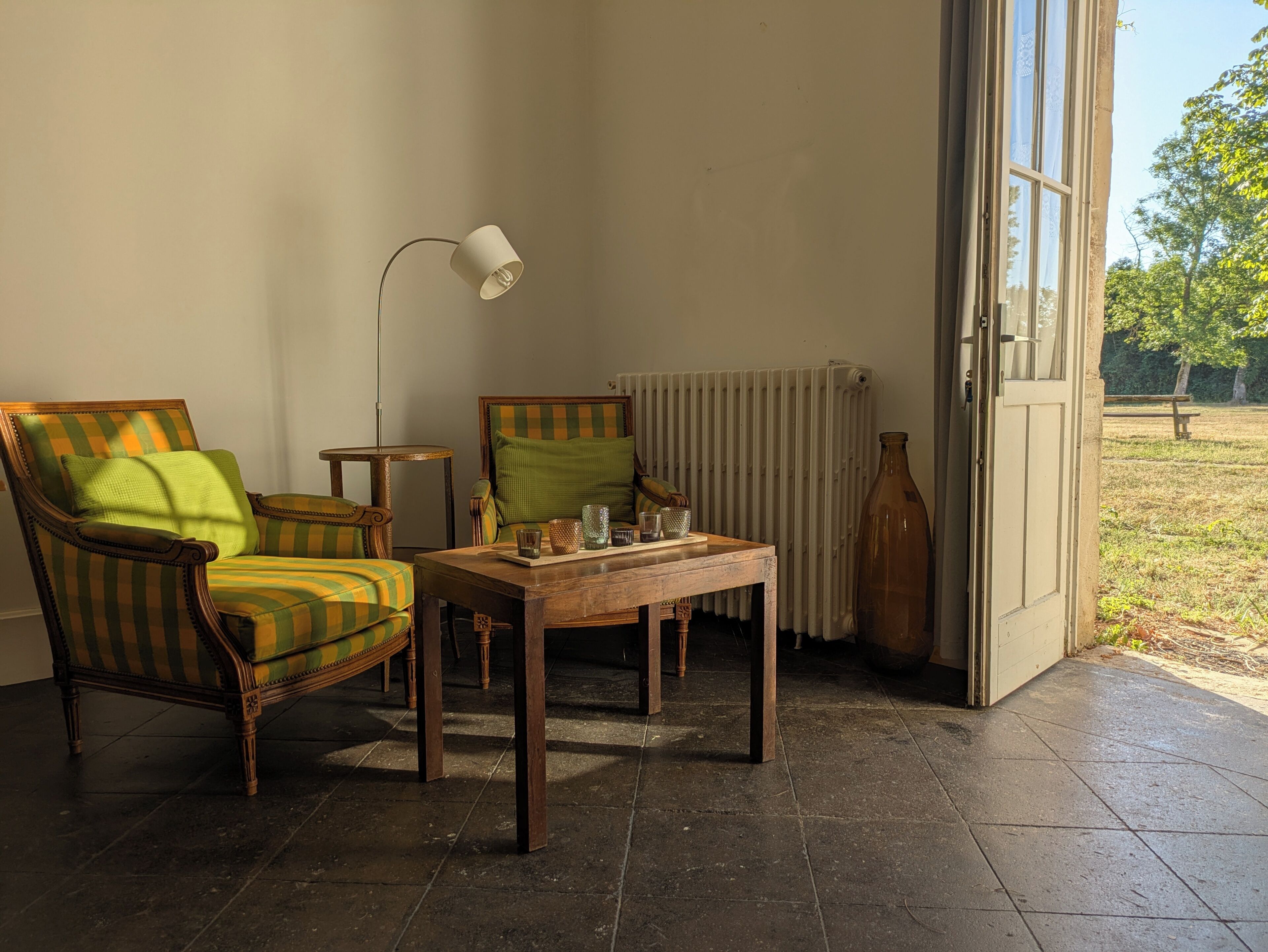 Una habitación con sillones a rayas, una mesita, una lámpara de pie y un radiador.