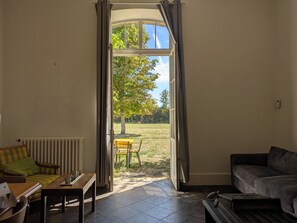 An open door leading to a patio with a table and chairs, a radiator, and a sofa inside a room. - La Lampisterie - Converted railway workshop on the edge of the Voie Verte (Saint Gengoux le National)