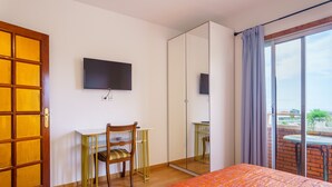 A bedroom with a bed, a desk, a chair, a TV, a large mirror, and a balcony with a table and chairs.