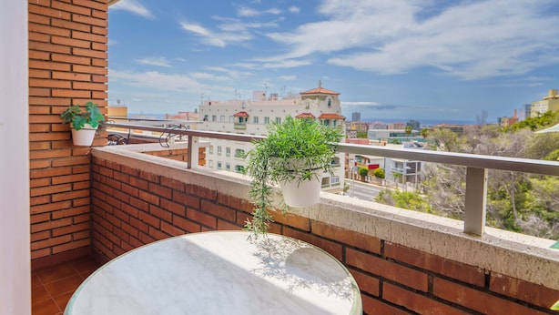 A balcony with a round table, potted plants, and a view of buildings and trees.
