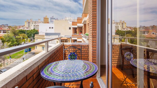 Un balcón con una mesa y sillas de cerámica, vista panorámica de la ciudad y una pared de ladrillo.