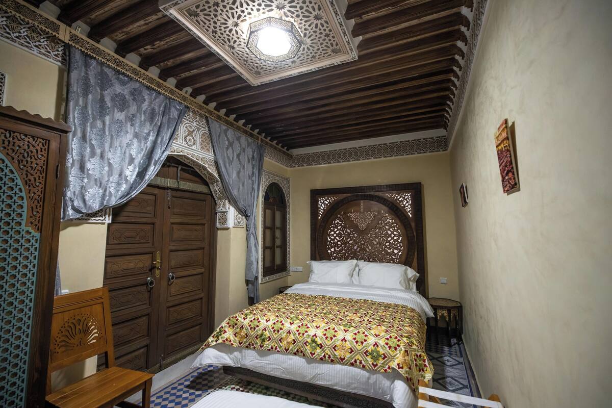 A traditional room with a bed, wooden furniture, and intricate ceiling design.