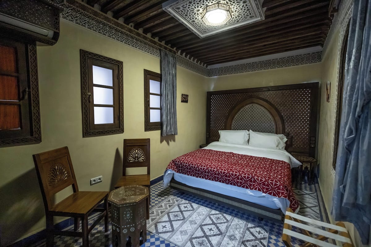 A traditional room with a patterned floor, a bed with a red and white bedspread, wooden furniture, and a decorative ceiling light.