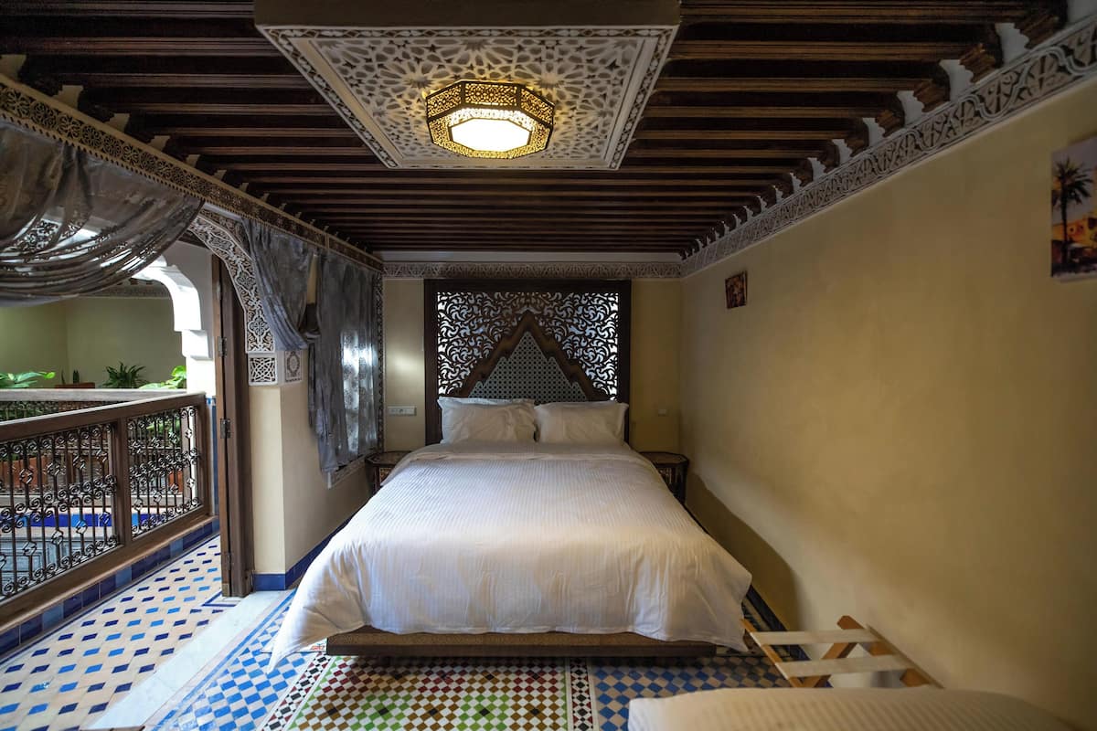 A bedroom with a large bed, a decorative ceiling light, and a view of a balcony with a railing.