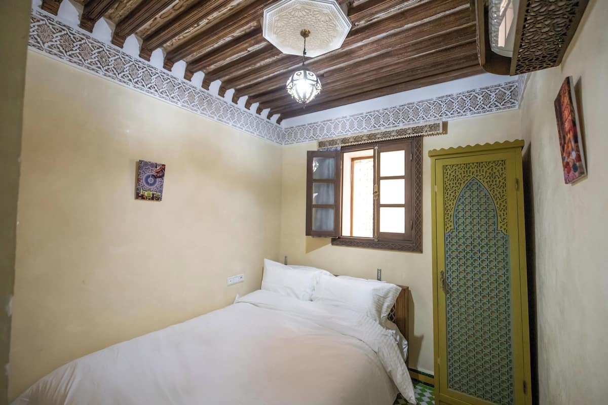 A bedroom with a bed, a window, and a door with intricate patterns.