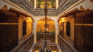 Een meerlaags interieur met sierlijke houten deuren en balustrades, een centrale decoratieve kolom en plantenbakken op balkons.