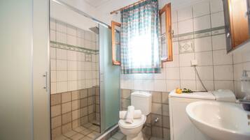 Un baño con ducha, inodoro, lavamanos y ventana con cortina.