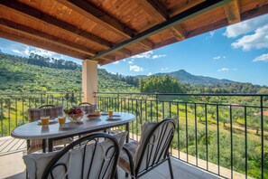 Un balcon avec une table dressée pour le petit-déjeuner, donnant sur un paysage verdoyant et luxuriant, parsemé de collines.