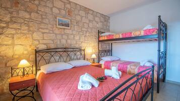 A bedroom with a bunk bed, a single bed, stone walls, a nightstand with a lamp, and towels on the beds.