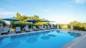 Une piscine entourée de verdure, avec des chaises longues et des parasols.