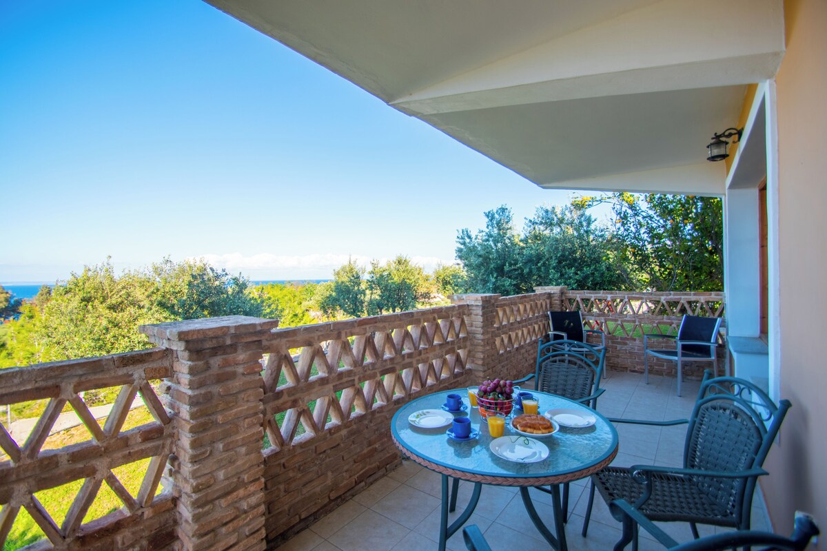 A patio with a round table and chairs, a view of the sea, and a brick wall.