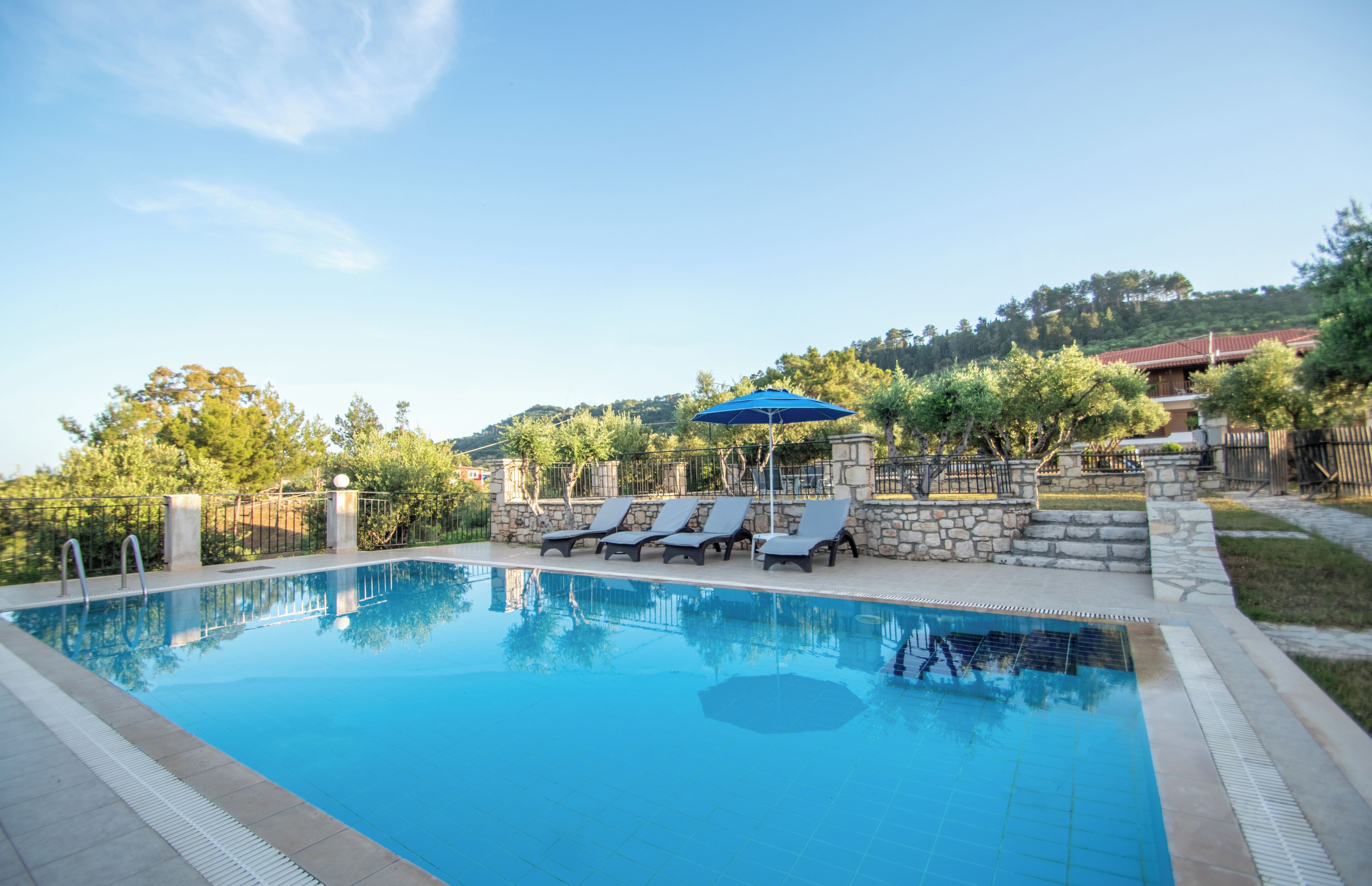 A clear swimming pool with lounge chairs and a stone wall.