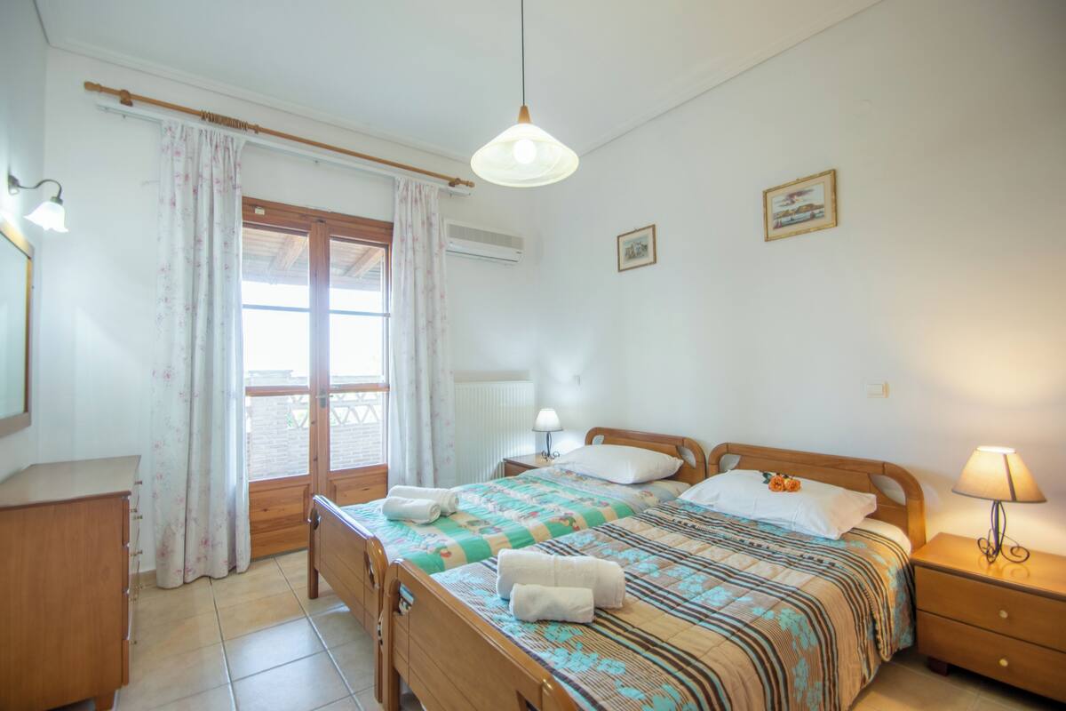 A bedroom with a wooden bed, a nightstand with a lamp, a window with curtains, and a radiator.