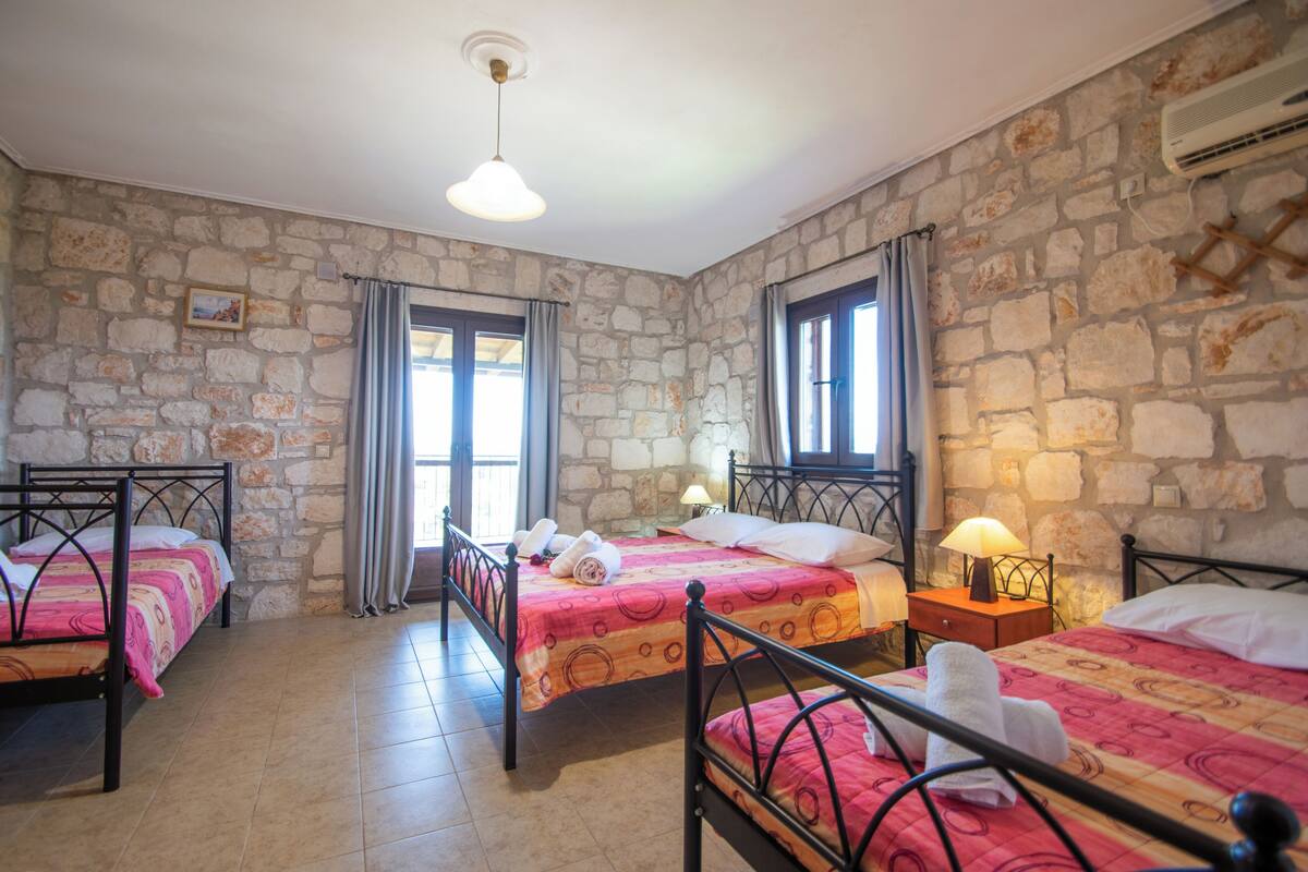 A room with three beds, stone walls, and a large window with curtains.