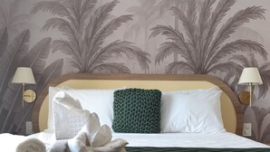 A hotel room with a bed, a green throw pillow, a white towel, and a wall with a palm tree pattern. - Santé Vivre L'Experience Livá OFICIAL (Búzios)