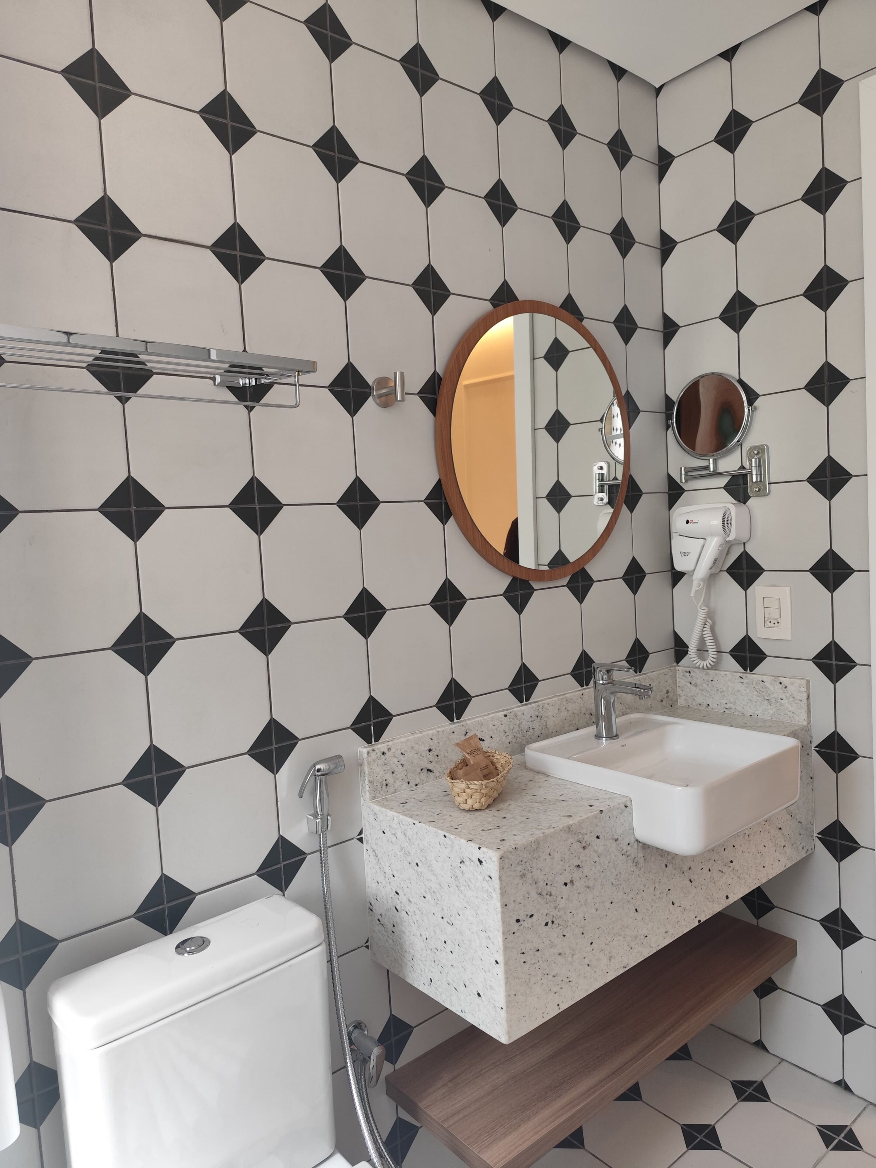 A bathroom with a white toilet, a sink with a speckled countertop, a wooden shelf, and a mirror with a wooden frame.
