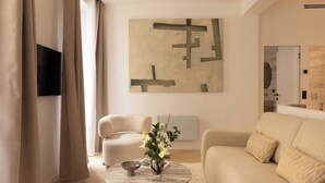Ett modernt vardagsrum med en beige soffa, ett runt soffbord med en vas med blommor, en platt-TV som är monterad på väggen och en stor, abstrakt tavla.