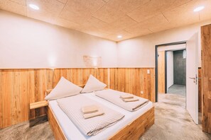 A room with a wooden bed, a wooden headboard, and a door leading to another room. - Möttelin Gut Hügle (Ravensburg)